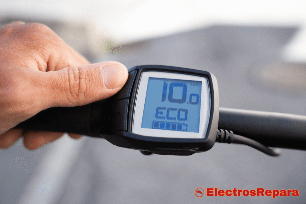 Primer plano del controlador de tu E-Bike ¿no?, mostrando una pantalla con 10.0 de velocidad, el modo de asistencia ECO y el nivel de batería de una bicicleta eléctrica. Una mano se acerca a los botones del manillar.