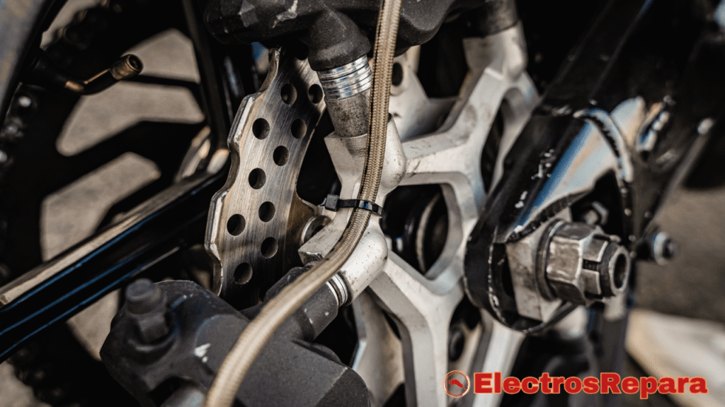 primer plano muestra el sistema de freno de disco de una motocicleta, incluyendo el disco perforado, la pinza y parte del basculante. Visualiza áreas críticas donde pueden surgir "ruidos moto eléctrica" relacionados con los frenos, como pastillas desgastadas o suciedad en el disco, esenciales para el diagnóstico y mantenimiento.
