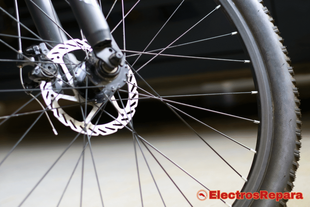 Primer plano de una rueda de bicicleta con un disco de freno visible, mostrando los radios y la llanta, en un entorno iluminado.