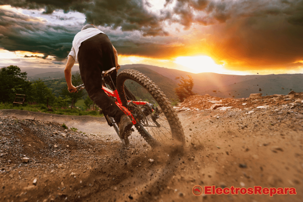 Un ciclista montando una bicicleta en una pista de tierra, levantando polvo mientras frena, con un paisaje montañoso y un atardecer dramático de fondo.