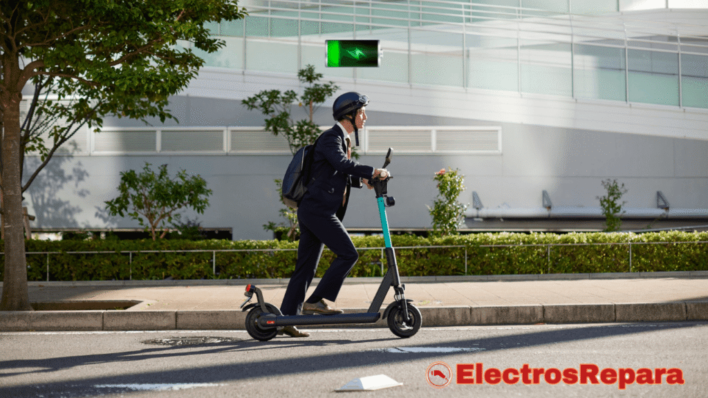 Esta imagen muestra a un hombre en traje y casco conduciendo un patinete eléctrico por una acera de la ciudad. Se observa un indicador de batería con carga casi completa en la parte superior derecha, lo que enfatiza la importancia de las Baterías para Patinete Eléctrico en su funcionamiento. El entorno sugiere un área urbana con edificios y árboles.