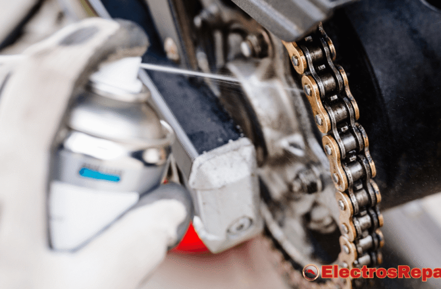 un proceso de lubricación de la cadena de tu bicicleta eléctrica. Una mano enguantada en blanco sostiene un bote de aerosol y aplica un lubricante directamente sobre la cadena. La cadena tiene un aspecto metálico brillante y está conectada al cassette y al motor de la bicicleta. Se puede ver claramente cómo el lubricante es rociado sobre los eslabones de la cadena. El fondo está ligeramente desenfocado, lo que dirige la atención hacia el proceso de lubricación de la cadena de tu bicicleta eléctrica.