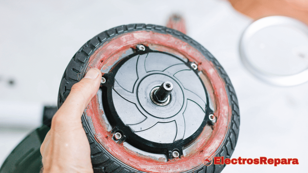 La imagen muestra una vista de cerca de una rueda de patinete eléctrico que está siendo examinada por una persona. Se puede ver claramente el motor eléctrico integrado en el centro de la rueda.
La persona está sosteniendo el conjunto del motor y la rueda, y se aprecian los seis tornillos que sujetan la carcasa del motor. También se nota un residuo de sellador de color rojo o suciedad acumulada en el borde exterior del motor, lo que podría indicar un proceso de limpieza o mantenimiento del motor. La foto ilustra la importancia de la revisión y el cuidado de los componentes principales de un patinete para garantizar su correcto funcionamiento.