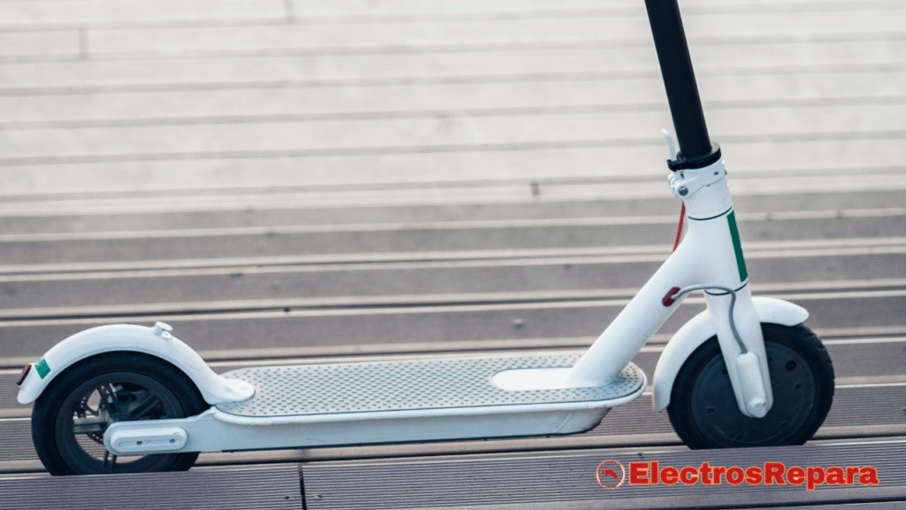 un patinete eléctrico blanco con detalles en colores, posiblemente de la bandera italiana (verde, blanco y rojo), estacionado de perfil sobre una superficie de tablas de madera al aire libre.